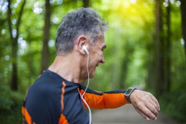 Side view of smiling senior man looking at smart watch in park - DIGF10306