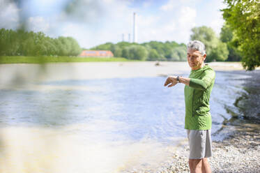 Aktiver älterer Mann prüft die Zeit, während er an einem sonnigen Tag am Flussufer steht - DIGF10313