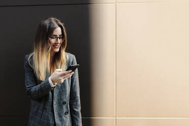 Lächelnde junge Geschäftsfrau schaut auf ihr Handy - MRRF00008