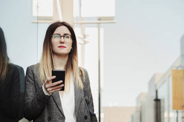 Portrait of young businesswoman with smartphone looking at distance - MRRF00014