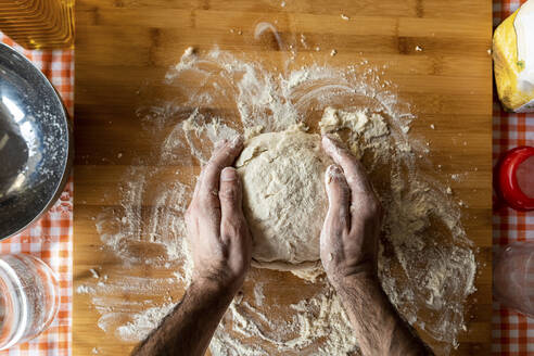 Man's hands kneading dough on wooden board, top view - WPEF02882