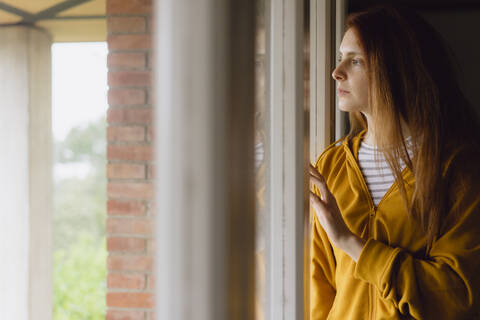 Nachdenkliche rothaarige Frau schaut aus dem Fenster, lizenzfreies Stockfoto