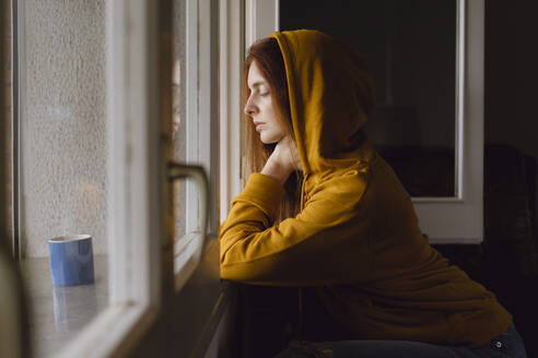 Frau mit gefütterter Jacke lehnt am offenen Fenster - AFVF06216