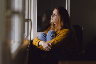 Pensive redheaded woman sitting at open window looking at distance - AFVF06225