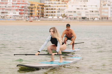 Young woman practicing paddleboarding with instructor on sea - MRRF00033