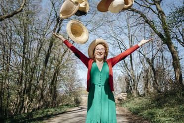 Porträt einer glücklichen reifen Frau, die Strohhüte in die Luft wirft - KMKF01308