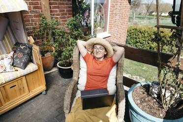 Porträt einer reifen Frau mit Laptop, die sich auf einer Terrasse entspannt - KMKF01313