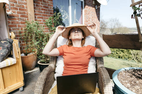 Ältere Frau mit Laptop entspannt auf Terrasse - KMKF01314