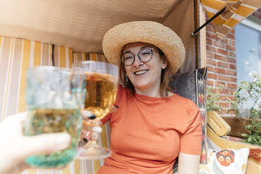 Porträt einer glücklichen reifen Frau auf einer Terrasse, die mit einem Glas Limonade anstößt - KMKF01321