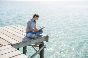 Frau sitzt auf einem Steg und liest eine Zeitschrift, Mallorca, Spanien - DIGF10331