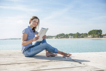 Frau sitzt auf einem Steg und liest eine Zeitschrift, Mallorca, Spanien - DIGF10334