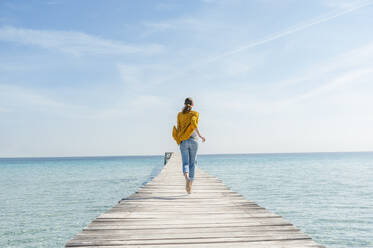 Back view of woman running barefoot on jetty, Mallorca, Spain - DIGF10335