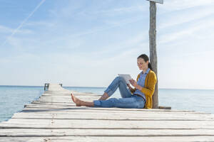 Frau sitzt auf einem Bootssteg und benutzt ein digitales Tablet, Mallorca, Spanien - DIGF10337