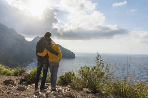 Rückenansicht eines Paares, das Arm in Arm steht und auf das Meer blickt, Mallorca, Spanien - DIGF10358