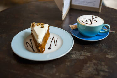 Eine Tasse Cappuchino und ein Stück Kuchen auf einem Tisch in einem Kaffeehaus - DIGF10370