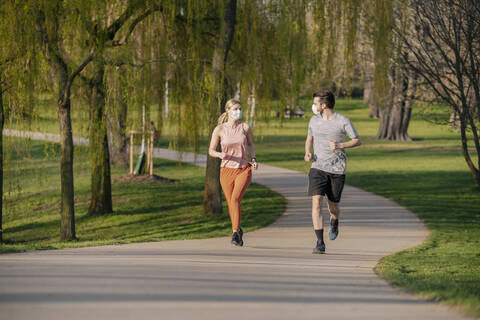Pärchen mit Gesichtsmasken beim Laufen auf dem Fußweg im Park, lizenzfreies Stockfoto