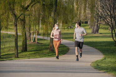 Couple wearing face masks while running on footpath at park - STDF00224