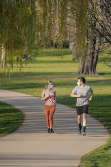 Paar trägt Gesichtsmasken beim Joggen auf dem Fußweg im Park - STDF00225