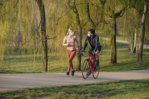 Mann fährt mit dem Fahrrad an einer Frau vorbei, die auf dem Fußweg in einem öffentlichen Park joggt, während COVID-19 - STDF00229