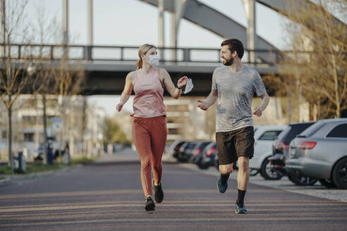 Junge Frau joggt, während sie einem Mann während der COVID-19-Pandemie eine Gesichtsmaske gibt - STDF00231