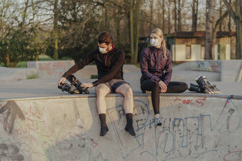 Young couple sitting with inline skates at skateboard park - STDF00234