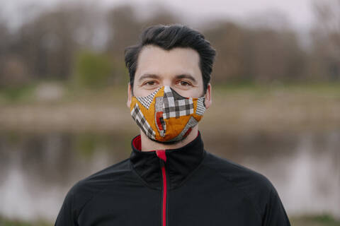 Portrait of confident young man wearing face mask at park during coronavirus stock photo