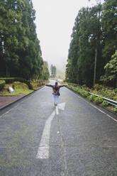 Full length rear view of young woman standing with arms outstretched on road, San Miguel, Azores, Portugal - FVSF00242