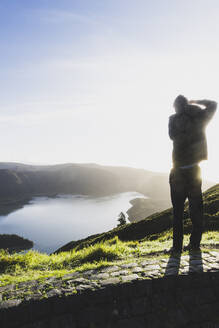 Rückansicht eines Mannes, der die Lagoa do Fogo gegen den Himmel bei Sonnenuntergang fotografiert, San Miguel, Azoren, Portugal - FVSF00246