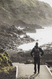 Rückansicht eines Mannes in voller Länge mit Blick auf die felsige Küste bei Ponta da Ferraria, San Miguel, Azoren, Portugal - FVSF00250
