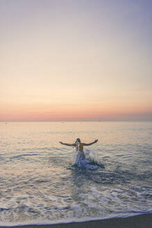 Teenager-Mädchen genießt beim Spritzen von Wasser im Meer während des Sonnenaufgangs - FVSF00265