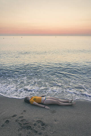 Full length of teenage girl lying on shore at beach during sunrise stock photo