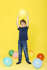 Full length portrait of smiling boy holding balloon against yellow background - JRFF04420