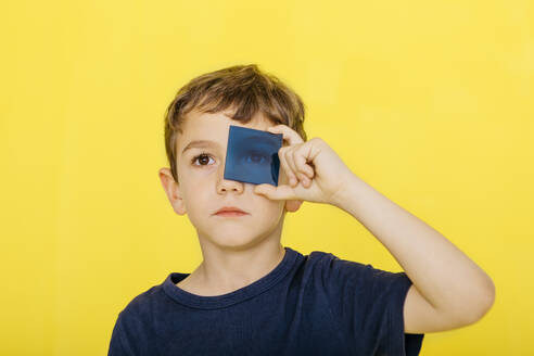 Nahaufnahme eines niedlichen Jungen, der ein blaues Acrylglas vor gelbem Hintergrund hält - JRFF04431