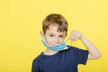 Porträt eines lächelnden Jungen, der eine Gesichtsmaske trägt und vor einem gelben Hintergrund steht - JRFF04437