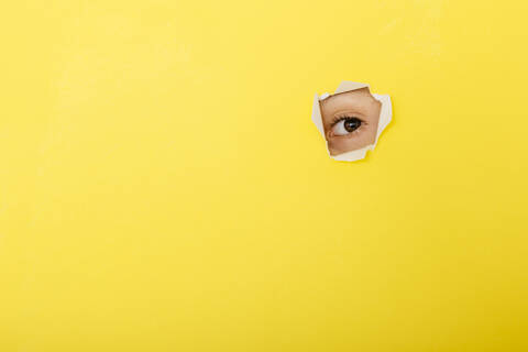 Nahaufnahme eines Jungen, der durch zerrissenes gelbes Papier schaut, lizenzfreies Stockfoto