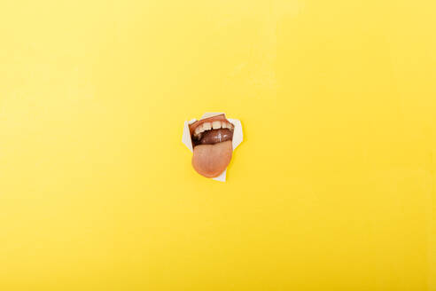 Close-up of boy sticking out tongue through torn yellow paper - JRFF04442