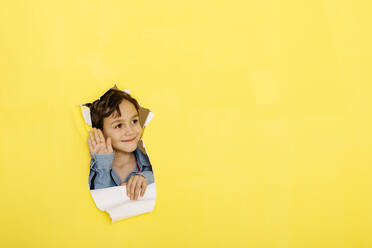 Lächelnder, winkender Junge, der durch zerrissenes gelbes Papier wegschaut - JRFF04446