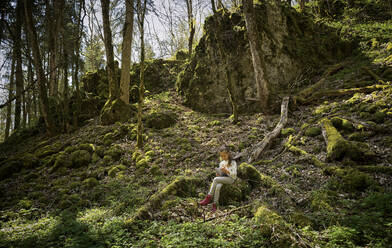 Mädchen sitzt im Wald der Schwäbischen Alb und benutzt ein digitales Tablet beim Wanderwochenende - DIKF00477