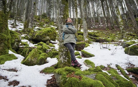 Frau lehnt an einer Buche im Nordschwarzwald mit Schneeresten im Frühling, lizenzfreies Stockfoto