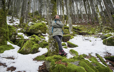 Frau lehnt an einer Buche im Nordschwarzwald mit Schneeresten im Frühling - DIKF00486