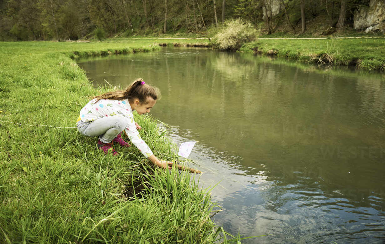 Girl puts his self-made toy boat into river in forest stock photo