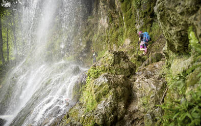 Geschwister wandern auf einer Felsformation unter dem Uracher Wasserfall im Wald - DIKF00495