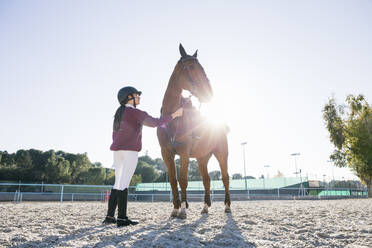 Gegenlicht Teenager-Mädchen stehend mit Kastanien Pferd auf dem Trainingsplatz gegen klaren Himmel - ABZF03102