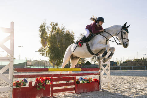 Teenage girl riding white horse while training for obstacle course on ranch - ABZF03111