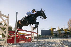Niedriger Blickwinkel von Jockey reitet Pferd über Hürde auf Trainingsgelände gegen klaren Himmel - ABZF03112
