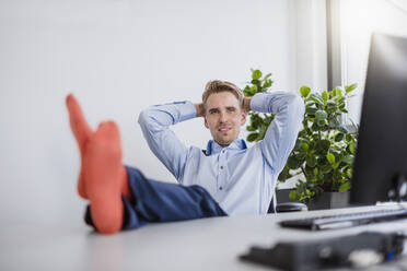 Lächelnder Geschäftsmann sitzt im Büro mit den Füßen auf dem Schreibtisch - DIGF10371