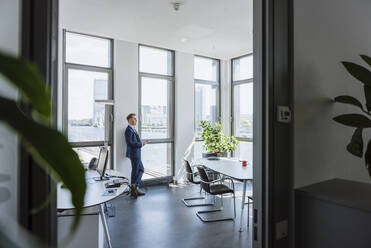 Businessman standing at thw window in office - DIGF10381