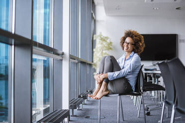 Smiling young businesswoman sitting at the window in conference room - DIGF10388