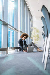 Young businesswoman sitting on the floor in conference room using laptop - DIGF10399