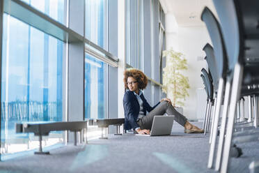 Young businesswoman sitting on the floor in conference room with laptop - DIGF10400